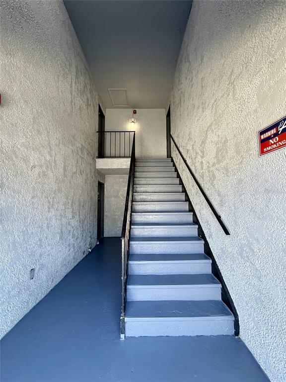 An indoor stairwell with gray painted steps, textured white walls, and a black metal railing — 4795 S TEXAS AVENUE UNIT 4795C, ORLANDO, FL