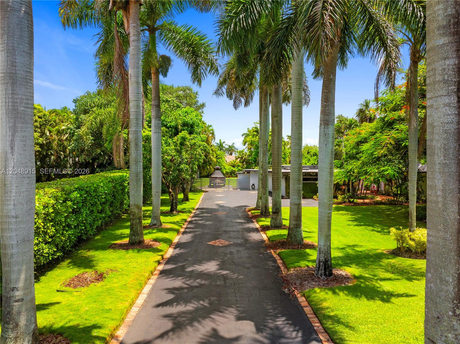 A paved driveway lined with tall palm trees leads toward a house and gate — 8735 SW 122nd St, Miami FL 33176, MIAMI, FL