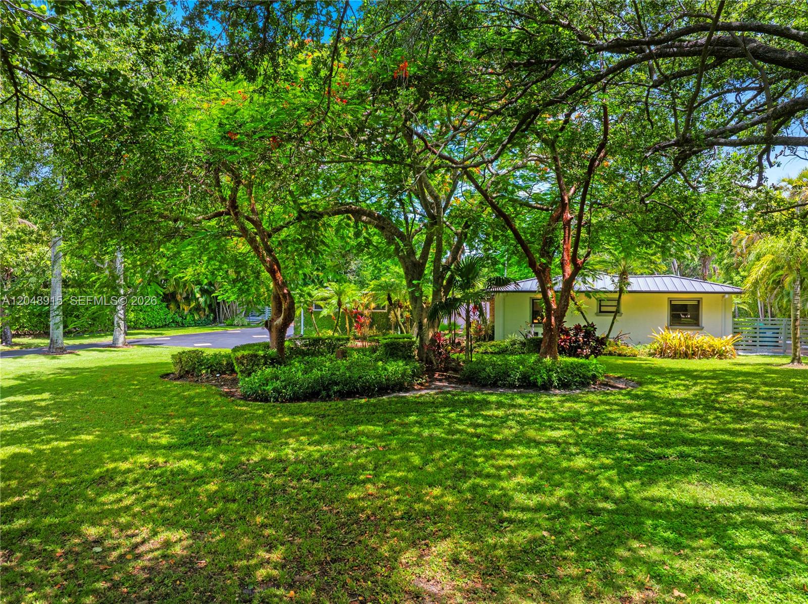 A grassy yard features mature trees and a small house with a metal roof — 8735 SW 122nd St, Miami FL 33176, MIAMI, FL