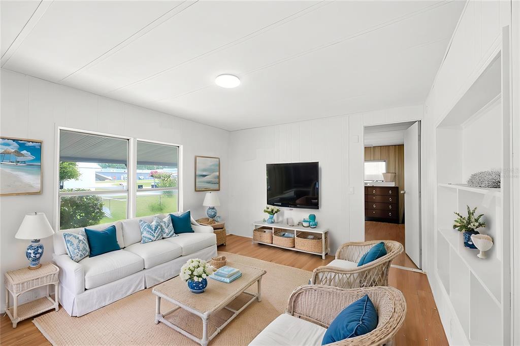 A bright living room features white walls, a white sofa, wicker chairs, and wood flooring — 7321 WINDY WAY, BROOKSVILLE, FL