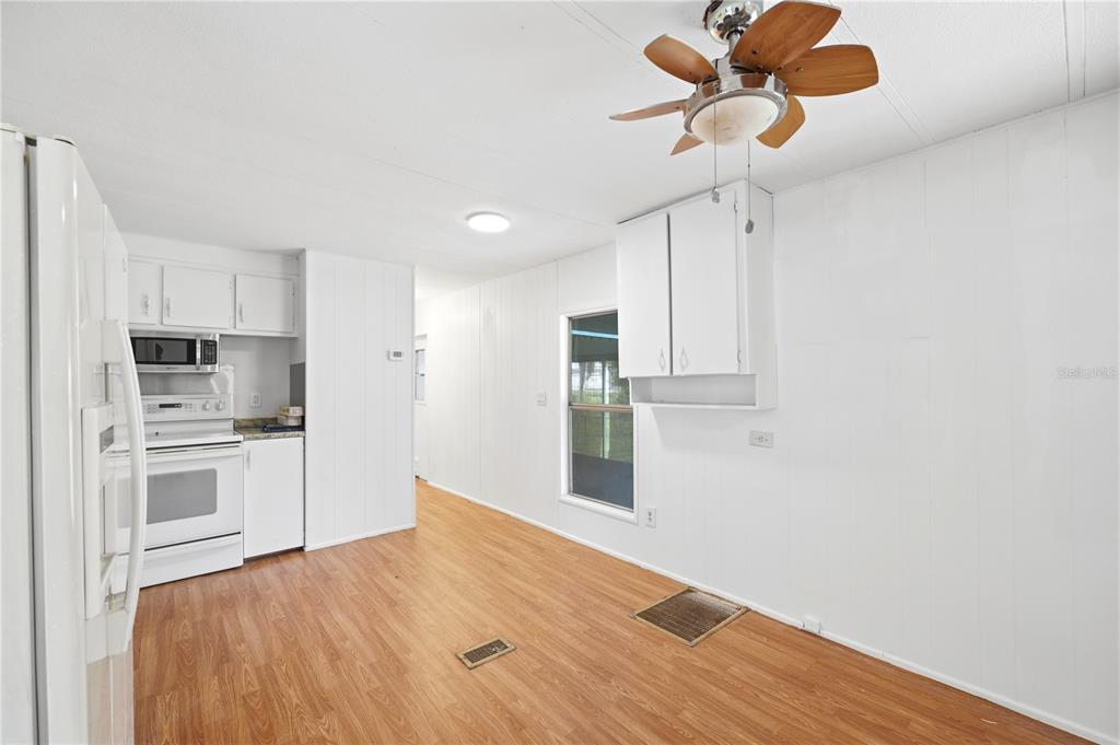 A kitchen and dining area with white cabinets, wood-look flooring, and a ceiling fan — 7321 WINDY WAY, BROOKSVILLE, FL