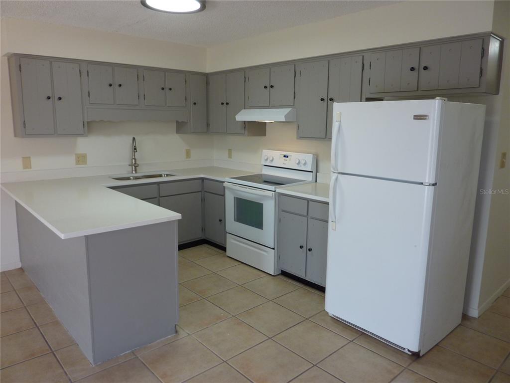 A kitchen features gray cabinets, white countertops, white appliances, and light-colored tile flooring — 1154 FAIRWAY DR, LAKELAND, FL