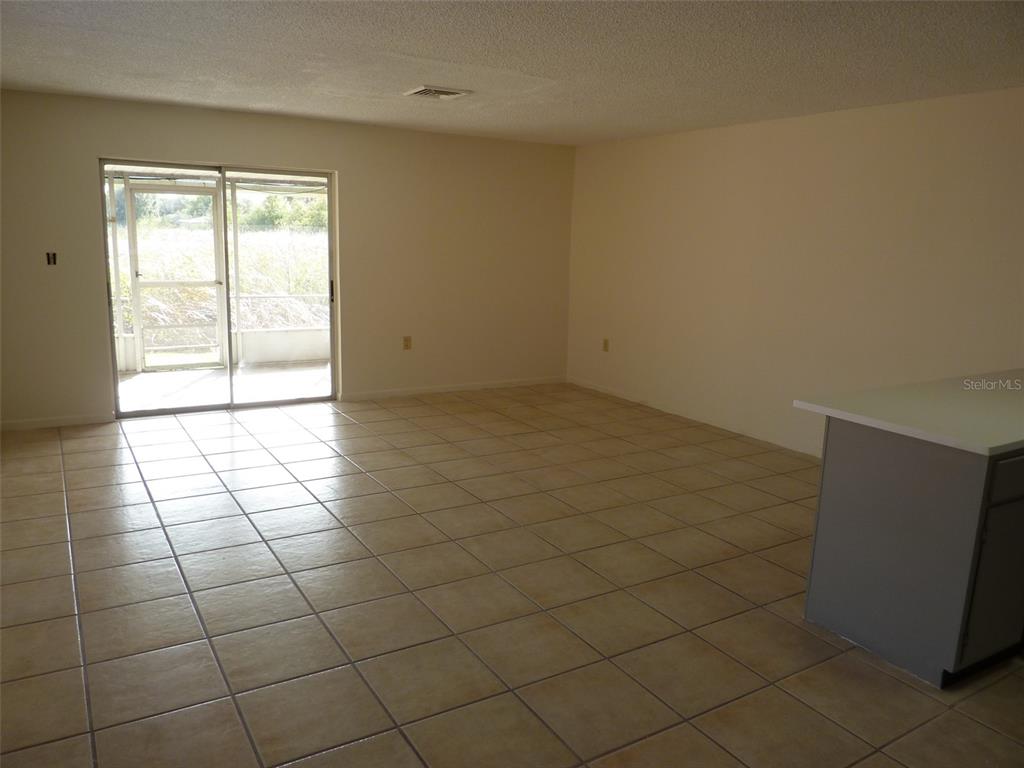 An empty living area with beige tile flooring, light walls, and a sliding glass door — 1154 FAIRWAY DR, LAKELAND, FL