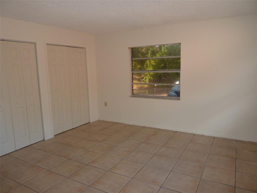 An empty room with beige tile flooring, white walls, two closet doors, and a window — 1154 FAIRWAY DR, LAKELAND, FL