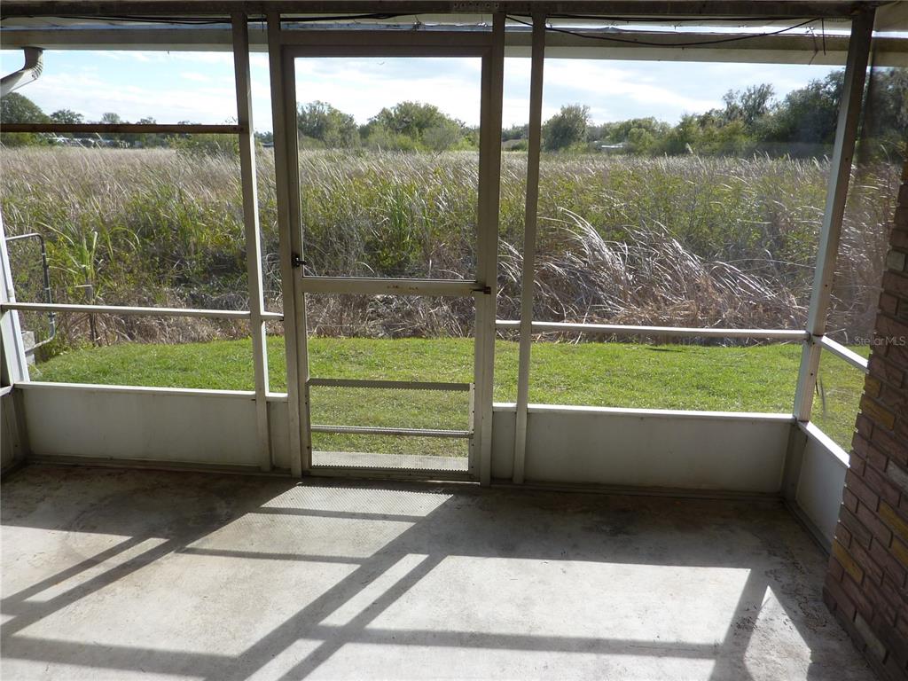 A screened-in porch with a concrete floor overlooks a grassy yard and tall marsh grass — 1154 FAIRWAY DR, LAKELAND, FL