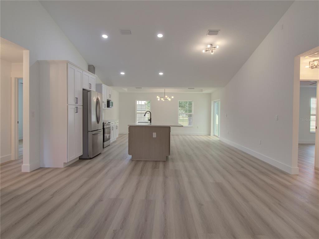 A bright, open-concept kitchen and living area features white cabinetry, a central island, and wood-look flooring — 9721 BAHIA ROAD, OCALA, FL