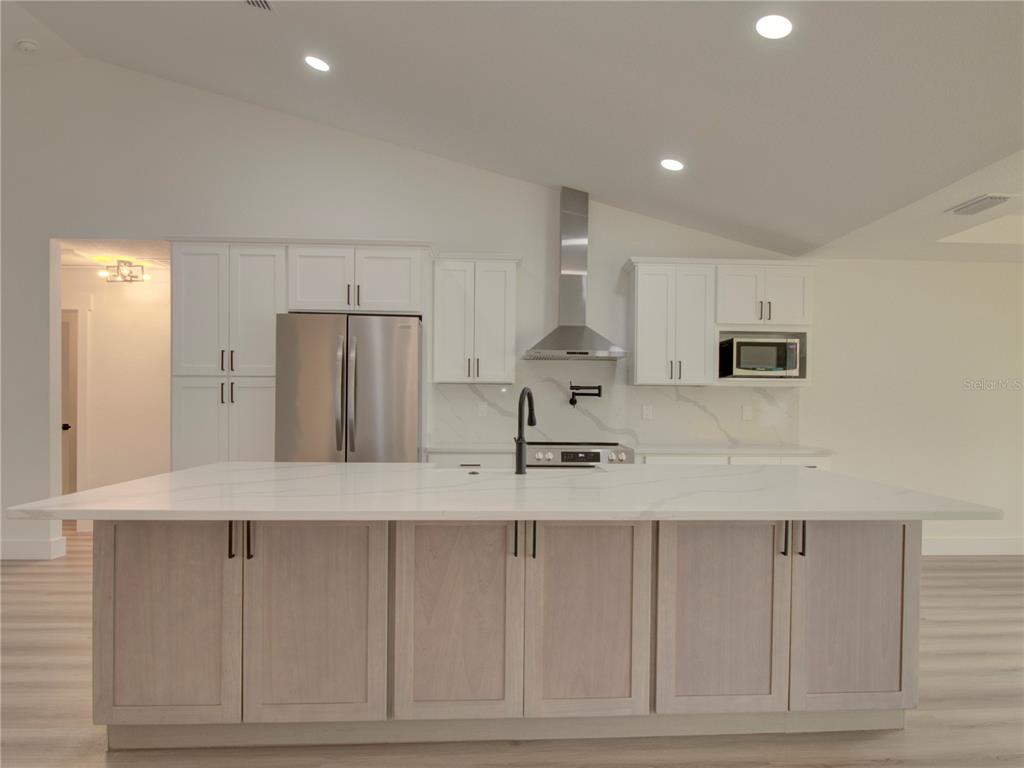 A kitchen features a large white island, light wood cabinets, and stainless steel appliances — 9721 BAHIA ROAD, OCALA, FL