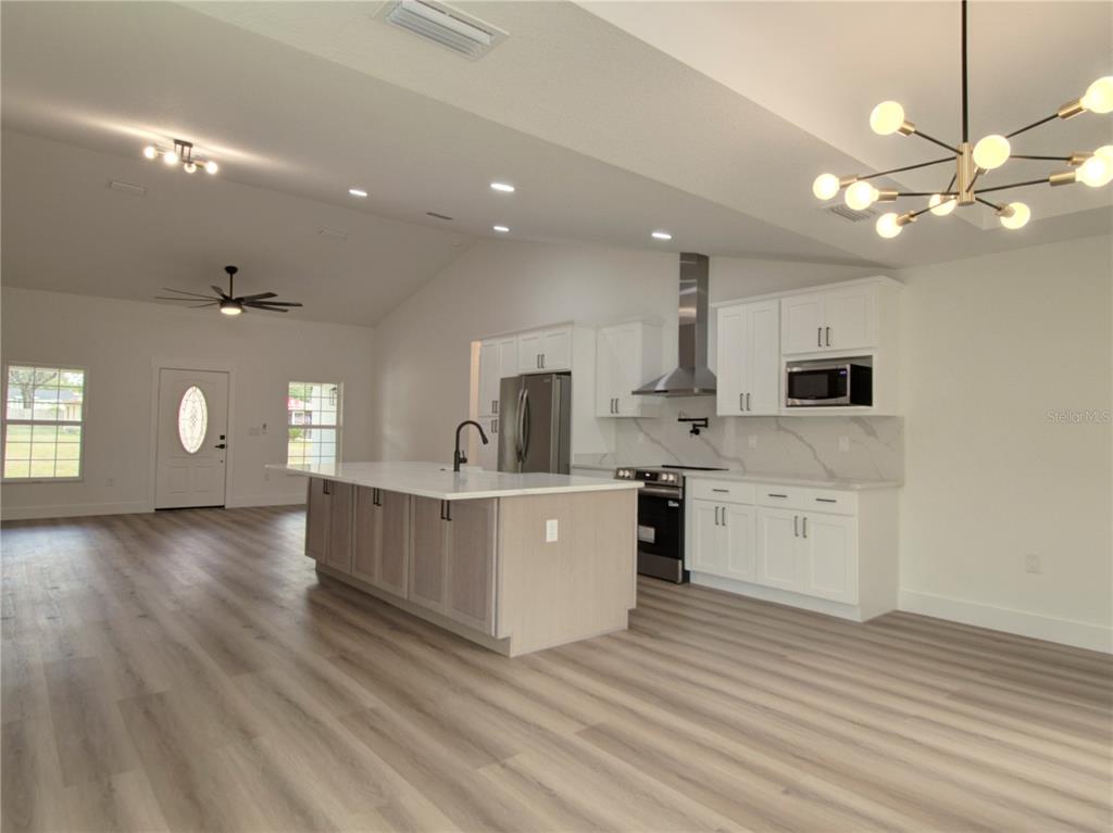 A modern kitchen features a large island, white cabinetry, stainless steel appliances, and wood-look flooring — 9721 BAHIA ROAD, OCALA, FL