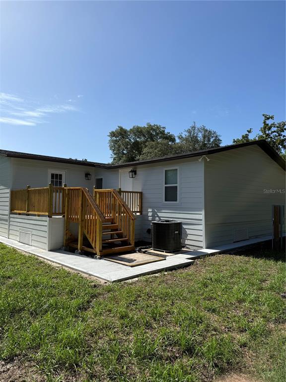 The exterior of a light-colored manufactured home features a wooden deck and an air conditioner — 15898 PEACE BOULEVARD, SPRING HILL, FL