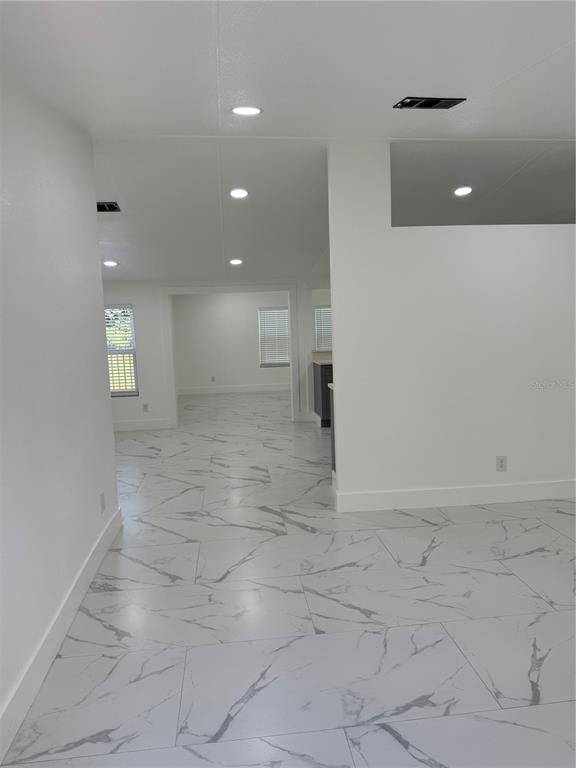 An interior view shows a white room with large-format marble-patterned tile flooring and recessed lighting — 15898 PEACE BOULEVARD, SPRING HILL, FL