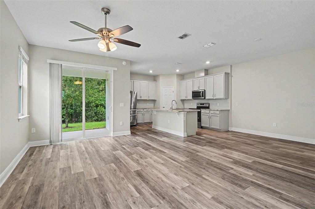 An open-concept kitchen and living area features light gray cabinetry, wood-look flooring, and sliding doors — 1427 BROAD WING LANE, WINTER PARK, FL