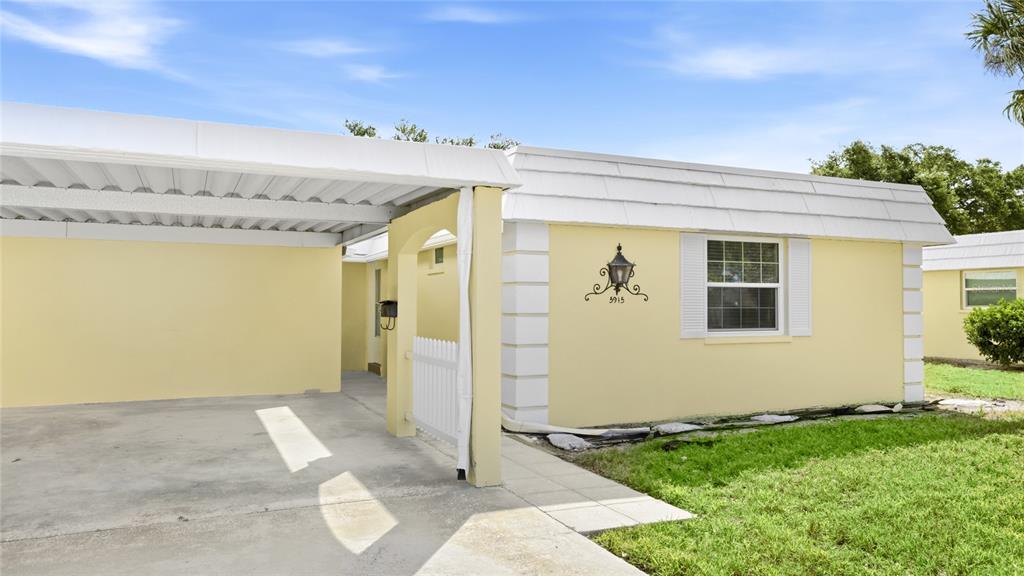 A yellow one-story house features a white carport, a small white gate, and a window — 5915 TIDEWOOD AVENUE UNIT 4, SARASOTA, FL