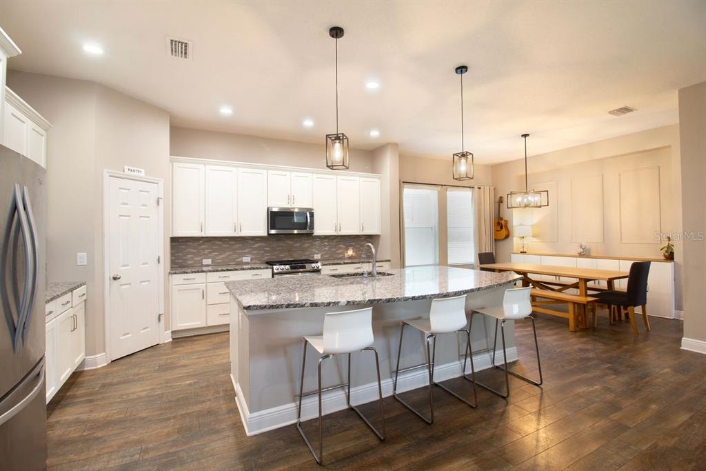 A kitchen with white cabinets, granite countertops, a center island, and an adjacent dining area — 14501 PROMENADE PARKWAY, ODESSA, FL