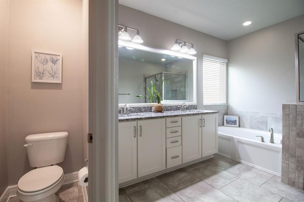 A bathroom featuring a double vanity with granite countertops, a soaking tub, and a toilet — 14501 PROMENADE PARKWAY, ODESSA, FL