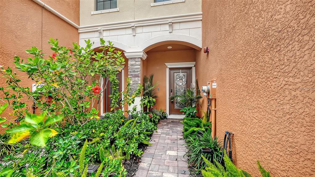A paved walkway leads to the front entrance of a stucco home with arched doorways — 20310 LAGENTE CIRCLE, VENICE, FL
