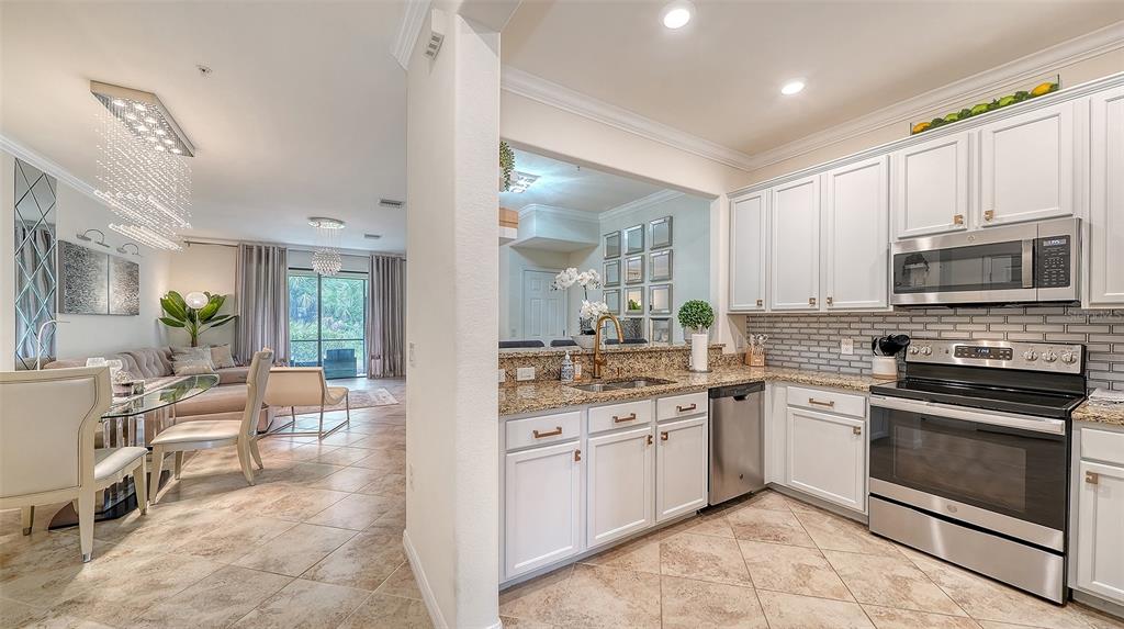 A kitchen with white cabinets and granite countertops opens into a dining and living area — 20310 LAGENTE CIRCLE, VENICE, FL