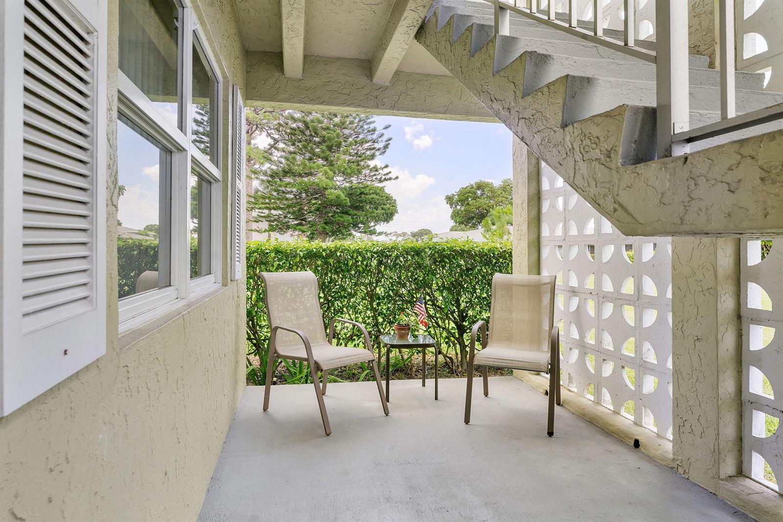 A covered patio features two chairs, a small table, and a concrete staircase overhead — 1041 Orange Terrace # 104, Delray Beach FL 33445, DELRAY BEACH, FL