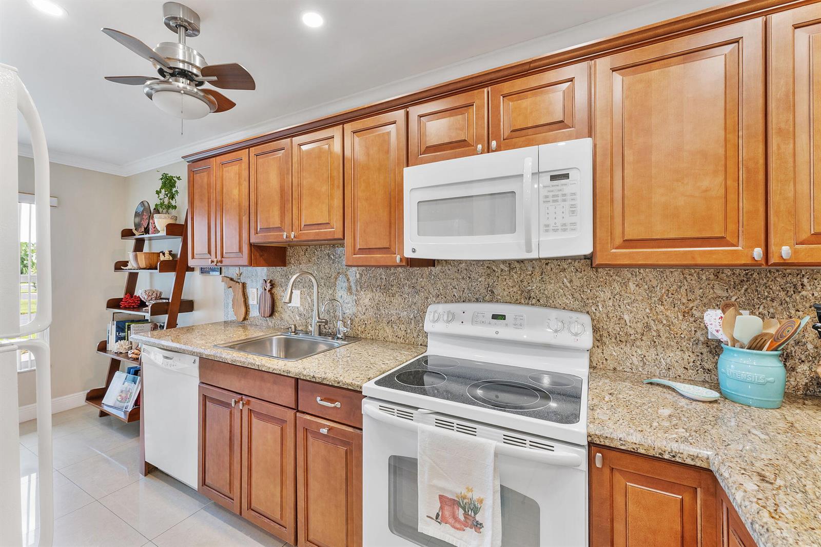 A kitchen features wood cabinets, granite countertops, white appliances, and a ceiling fan — 1041 Orange Terrace # 104, Delray Beach FL 33445, DELRAY BEACH, FL