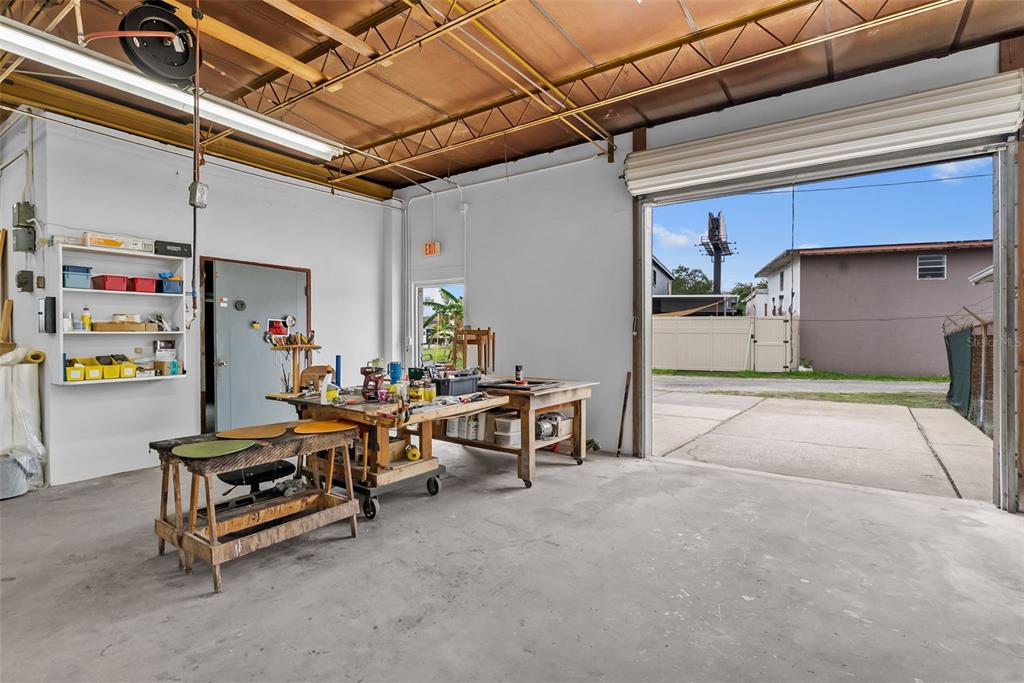 A workshop with concrete floors, workbenches, storage shelves, and an open roll-up garage door — 1444 19TH STREET N, ST PETERSBURG, FL