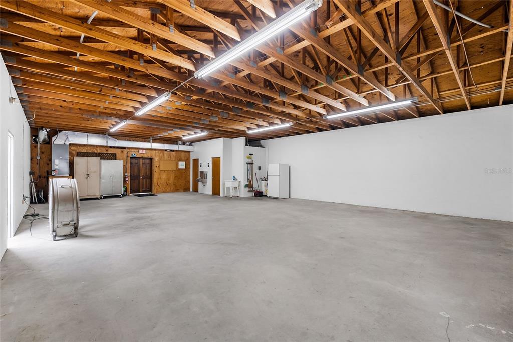 A large, open garage space features a concrete floor, exposed wooden rafters, and fluorescent lighting — 1444 19TH STREET N, ST PETERSBURG, FL