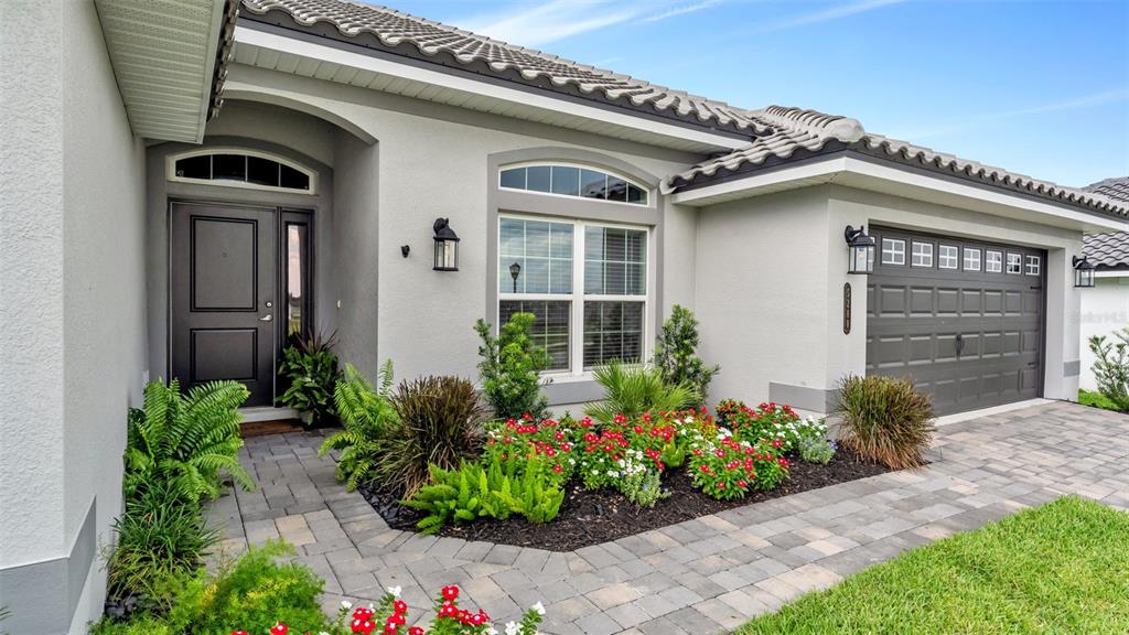 The exterior of a single-story house features a gray stucco facade, a dark garage door, and a landscaped garden bed — 5280 TENNESSEE RIDGE COURT, AUBURNDALE, FL