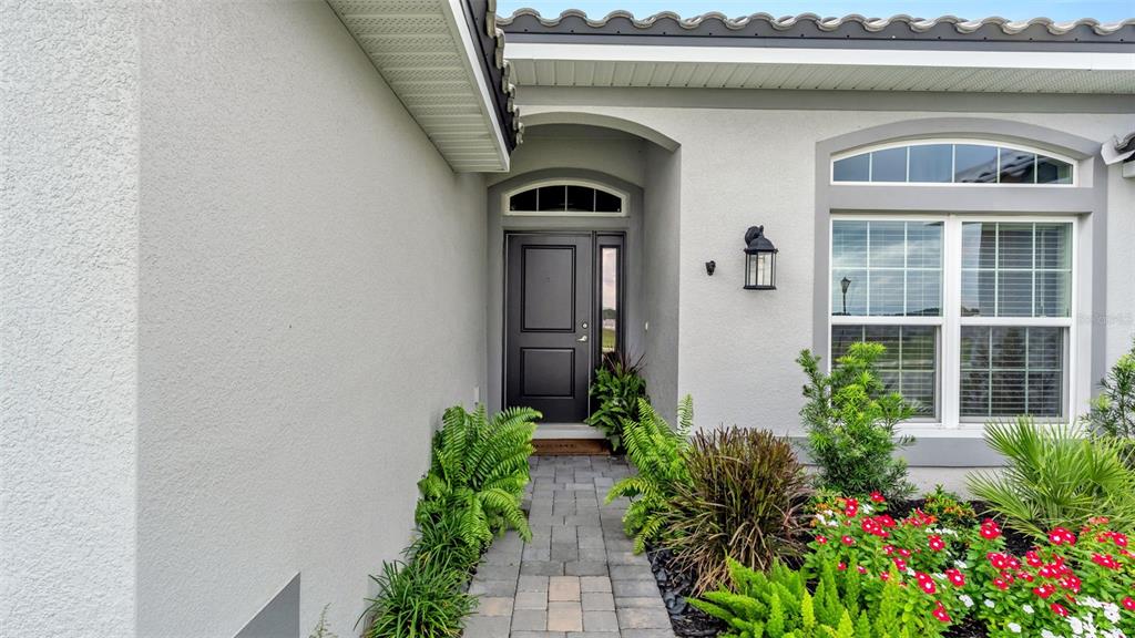 A paved walkway leads to the dark front door of a house with light stucco — 5280 TENNESSEE RIDGE COURT, AUBURNDALE, FL