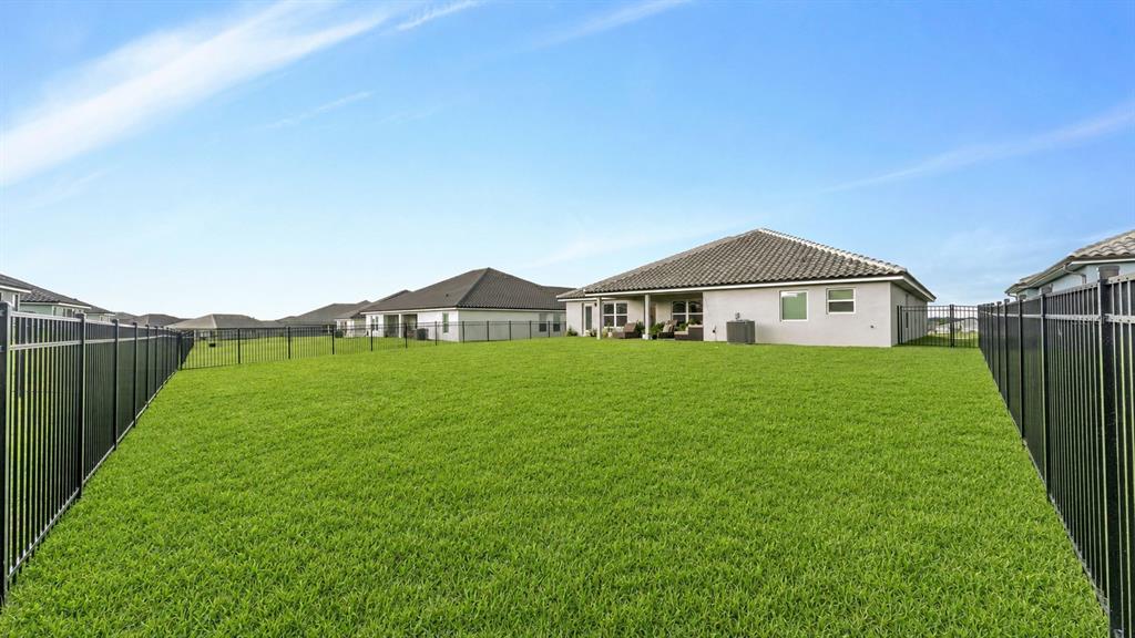 A large, fenced-in backyard with green grass extends behind a single-story suburban house — 5280 TENNESSEE RIDGE COURT, AUBURNDALE, FL