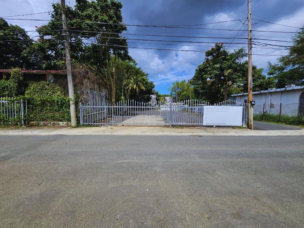 A gated entrance leads to a paved lot surrounded by trees and adjacent buildings — 19 CALLE ONGAY, BAYAMON, PR