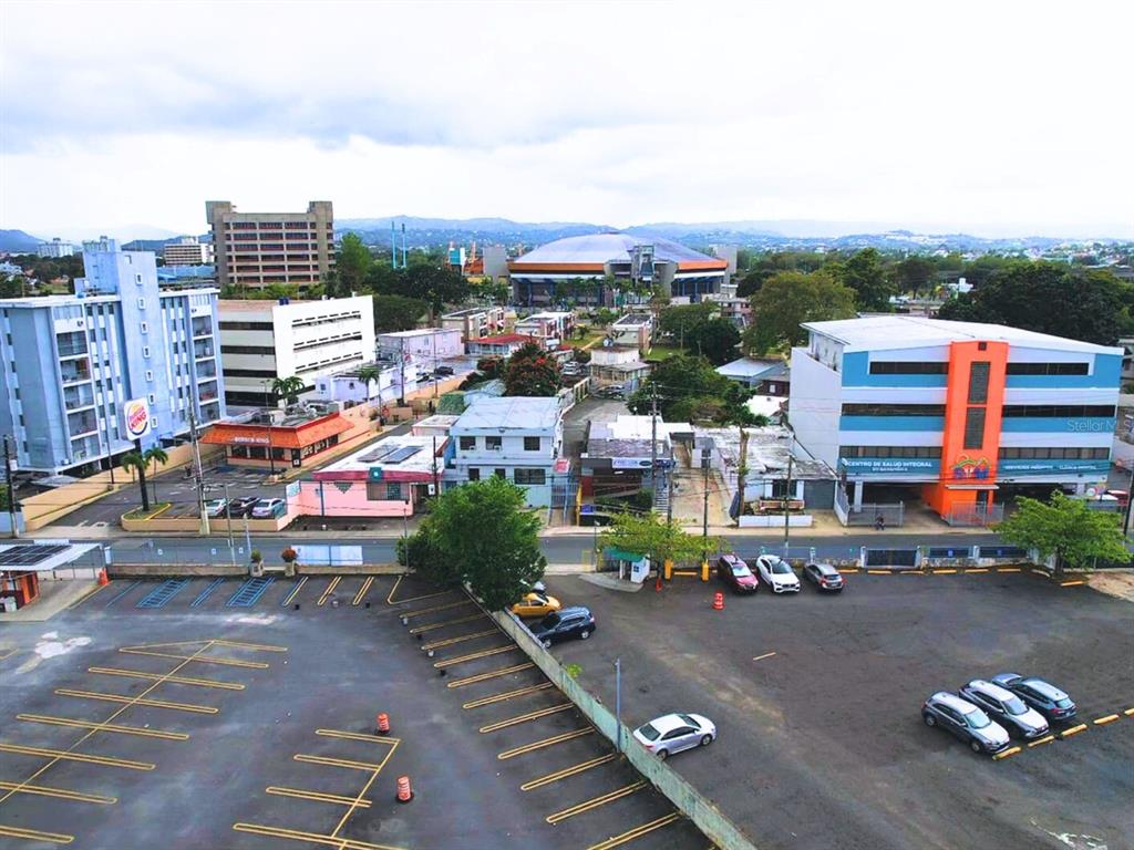 An aerial view shows a parking lot in the foreground with surrounding commercial buildings and mountains — 19 CALLE ONGAY, BAYAMON, PR