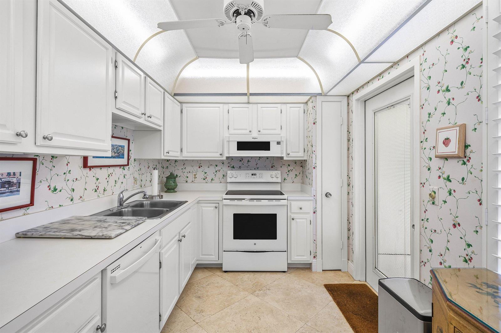 A kitchen with white cabinets, white appliances, floral wallpaper, and a vaulted ceiling light fixture — 4233 A Quail Ridge Drive N, Boynton Beach FL 33436, BOYNTON BEACH, FL