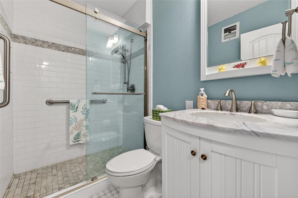 A bathroom features a glass-enclosed shower, a white vanity with a marble top, and blue walls — 3009 N HALIFAX AVENUE UNIT 1, DAYTONA BEACH, FL