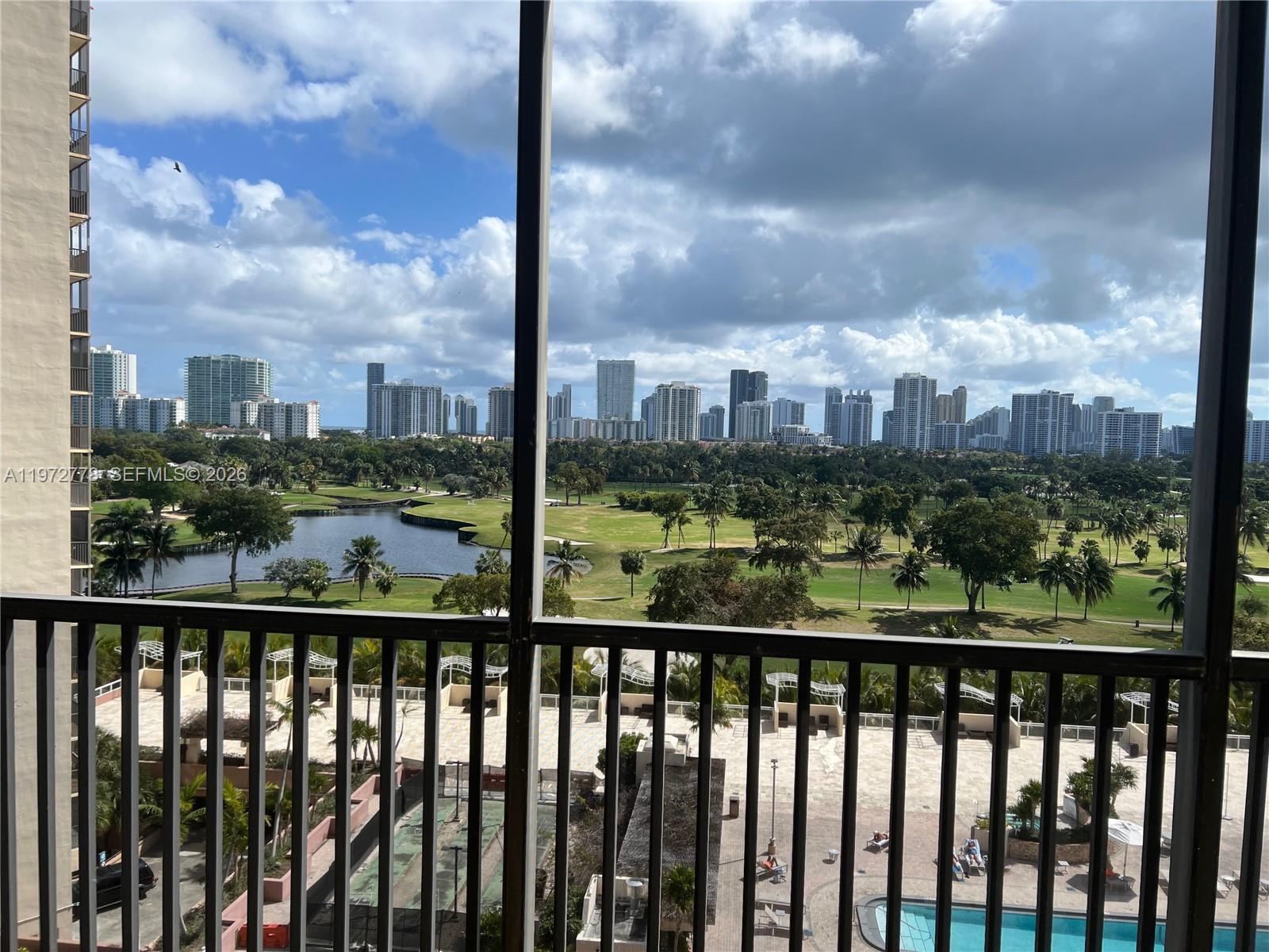 A balcony view overlooks a golf course, a lake, and a distant city skyline — AVENTURA, FL