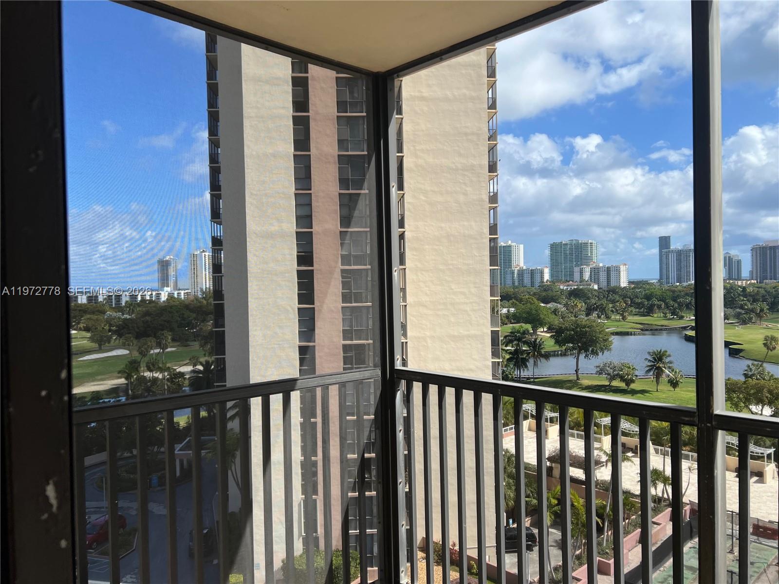 A balcony with a metal railing overlooks a golf course, a lake, and high-rise buildings — AVENTURA, FL