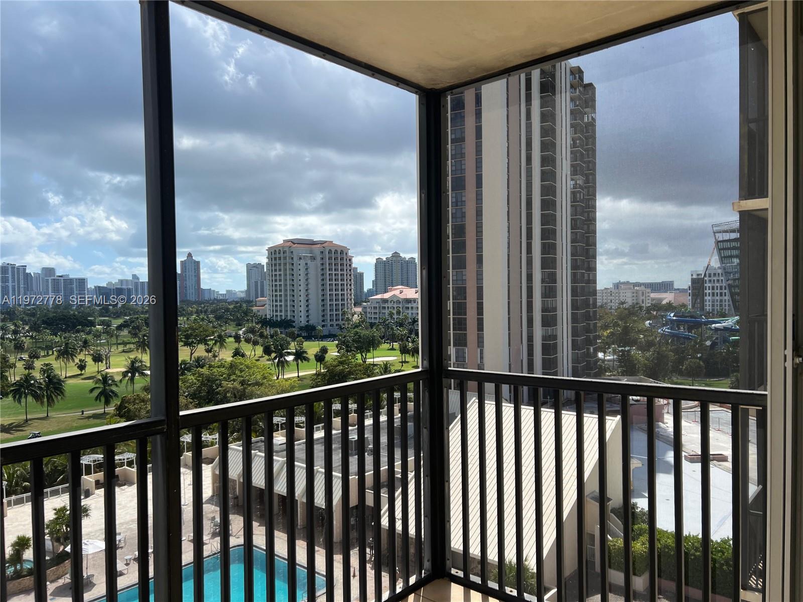 A screened balcony overlooks a golf course, swimming pool, and surrounding high-rise buildings — AVENTURA, FL