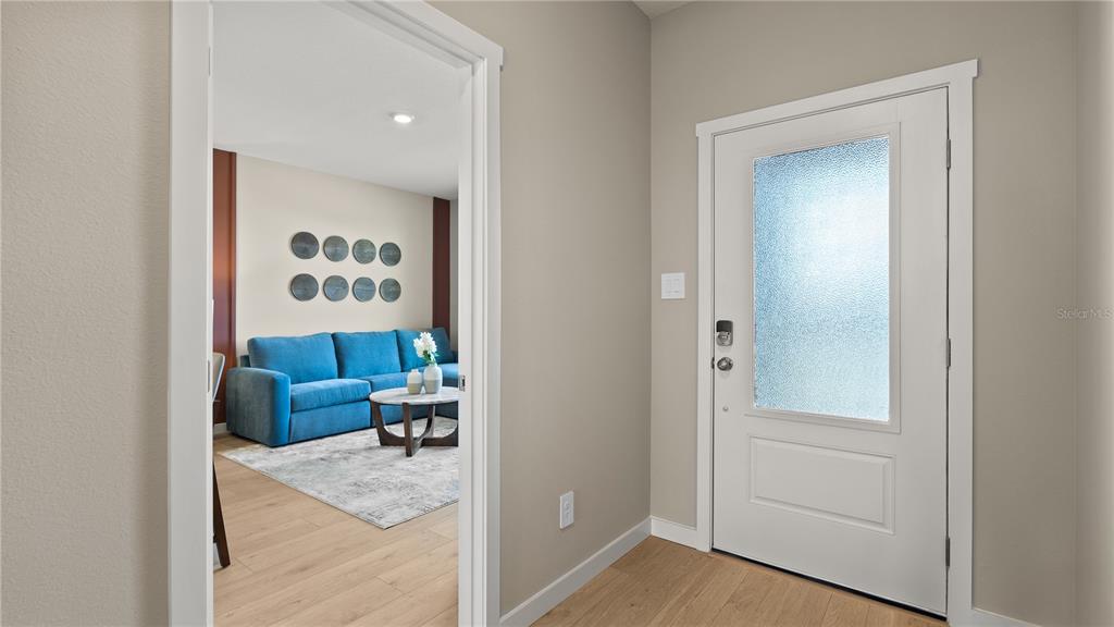 An entryway with light wood flooring leads into a living room with a blue sofa — 4891 WALTHAM FOREST DRIVE, DAVENPORT, FL