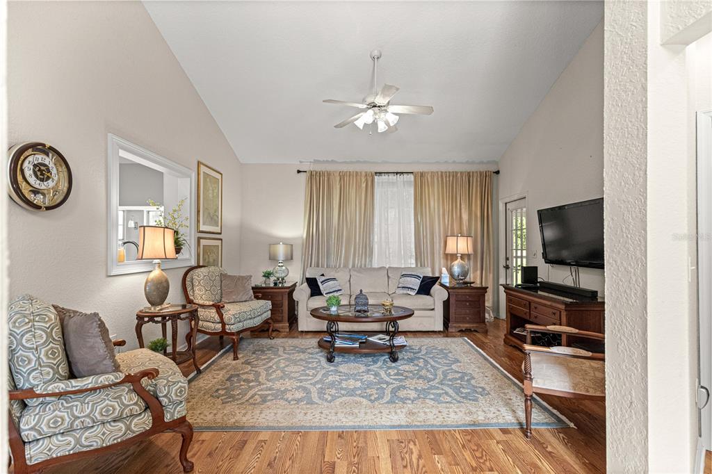 A living room features a vaulted ceiling, hardwood floors, a patterned rug, and traditional furniture — 11606 SW 75TH CIRCLE, OCALA, FL