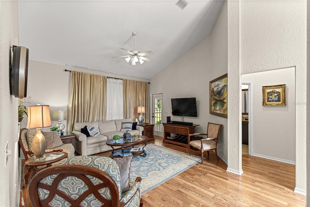A living room features vaulted ceilings, hardwood floors, a beige sofa, and a ceiling fan — 11606 SW 75TH CIRCLE, OCALA, FL