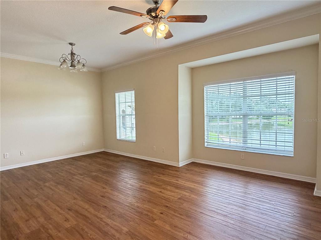 An empty room features wood-look flooring, a ceiling fan, a chandelier, and large windows — 407 EAGLE POND DRIVE UNIT 407, WINTER HAVEN, FL