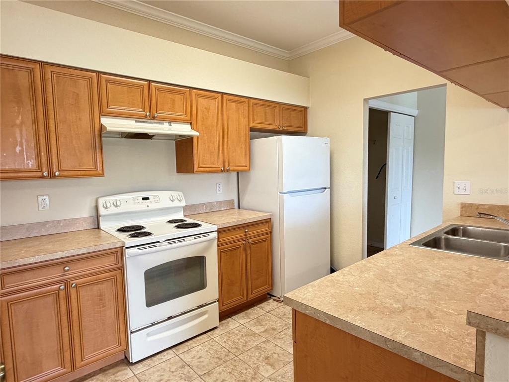 A kitchen features wood cabinets, white appliances, laminate countertops, and tile flooring — 407 EAGLE POND DRIVE UNIT 407, WINTER HAVEN, FL