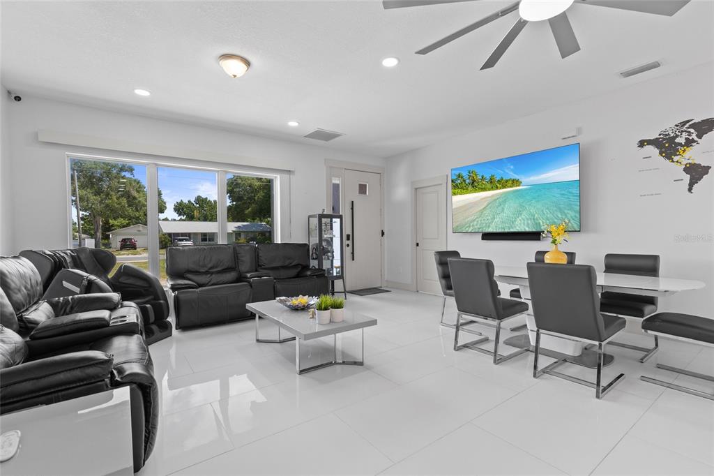 A bright living and dining area features white tile floors, black leather furniture, and a television — 11426 LAKEVIEW DRIVE, LEESBURG, FL