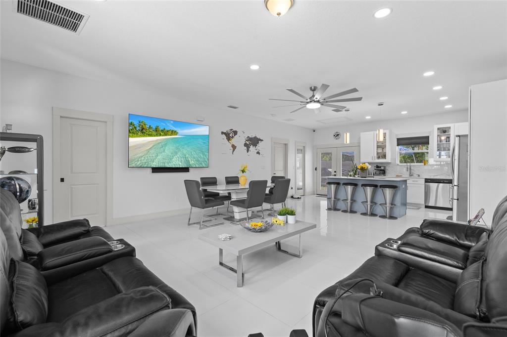 A modern open-concept living room and kitchen with white tile floors and black leather furniture — 11426 LAKEVIEW DRIVE, LEESBURG, FL