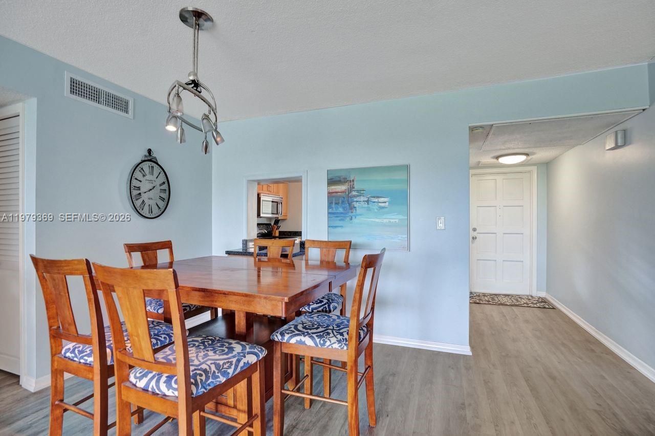 A dining area with a wooden table, patterned chairs, and a wall clock — 2651 S Course Dr # 203, Pompano Beach FL 33069, POMPANO BEACH, FL