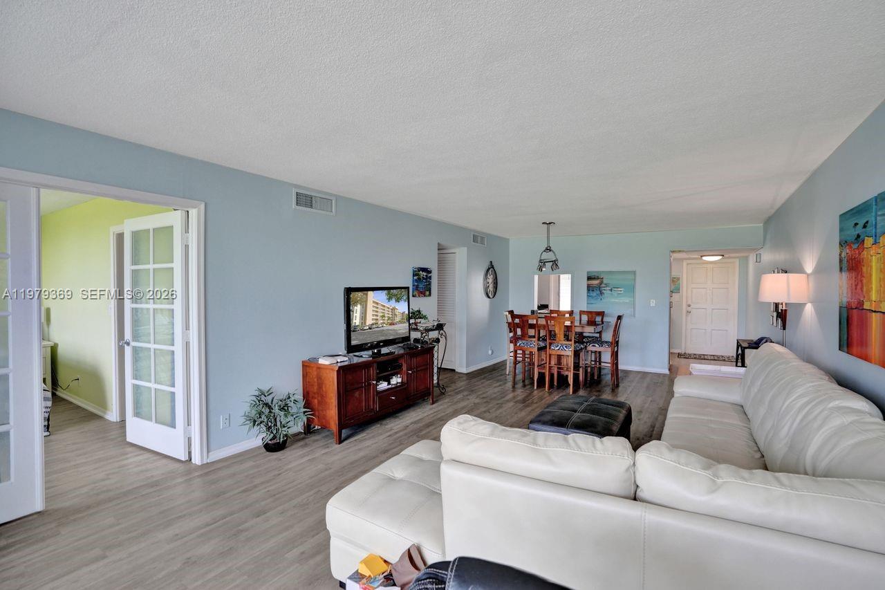 A living room with light blue walls, wood-look flooring, a white sofa, and a dining area — 2651 S Course Dr # 203, Pompano Beach FL 33069, POMPANO BEACH, FL