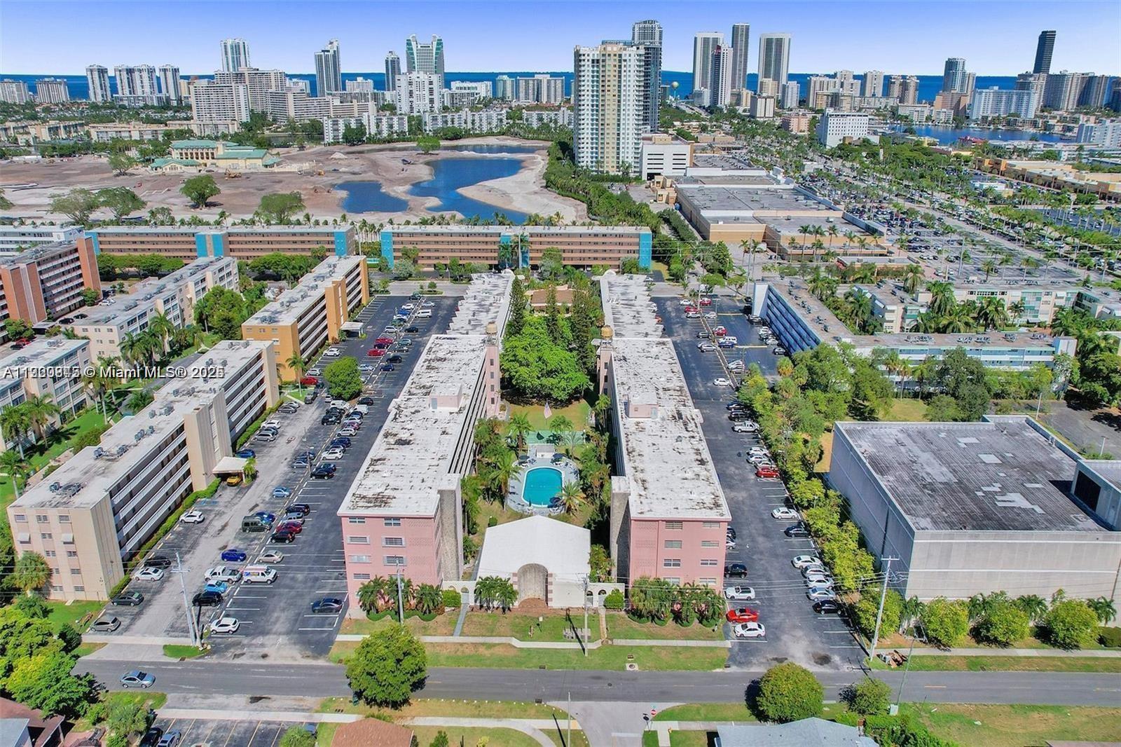 An aerial view shows two multi-story apartment buildings with a central pool and parking lots — 180 NE 12th Ave # 12E, Hallandale Beach FL 33009, HALLANDALE BEACH, FL