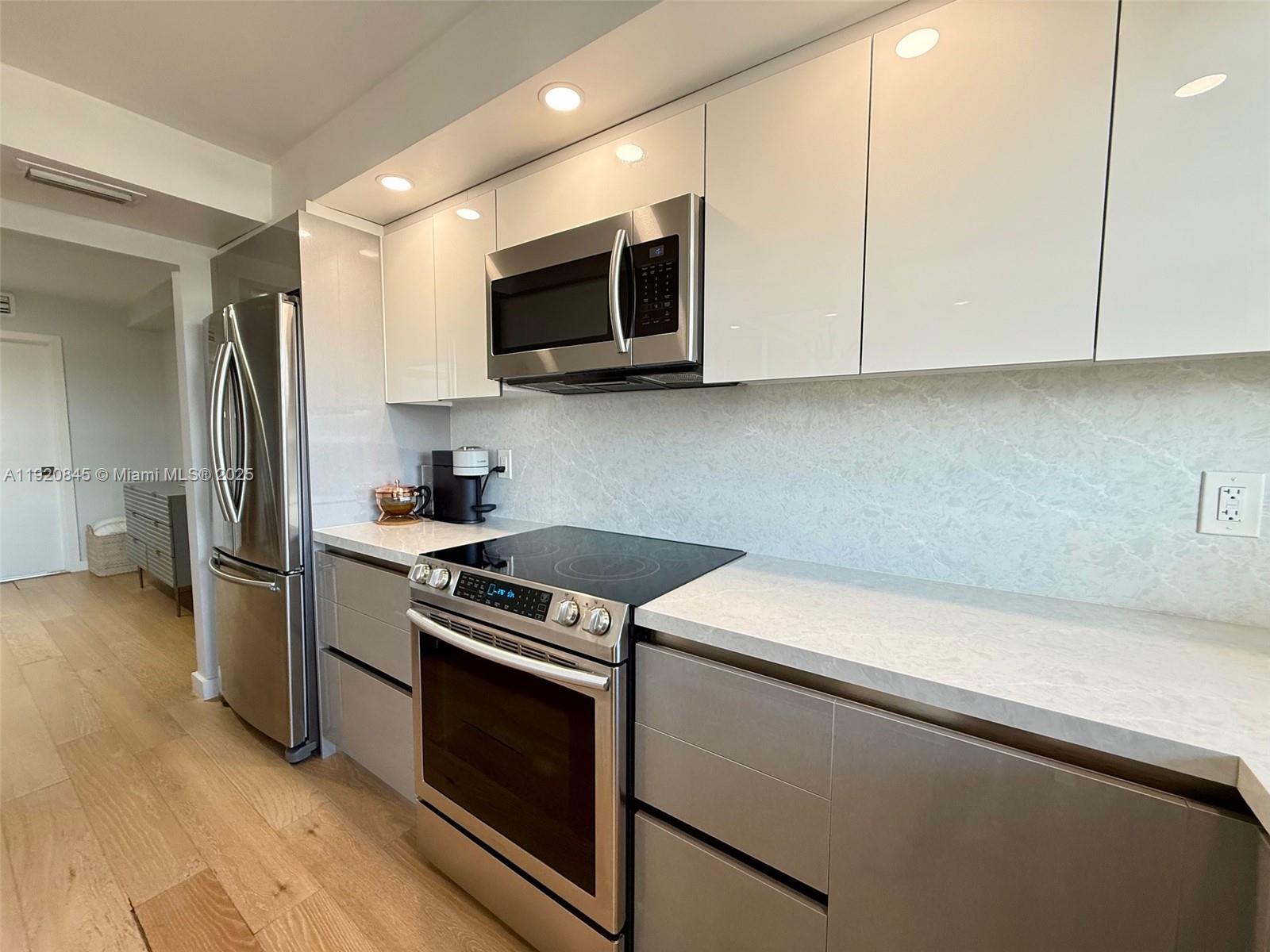 A modern kitchen features stainless steel appliances, white glossy cabinets, and light stone countertops — 180 NE 12th Ave # 12E, Hallandale Beach FL 33009, HALLANDALE BEACH, FL