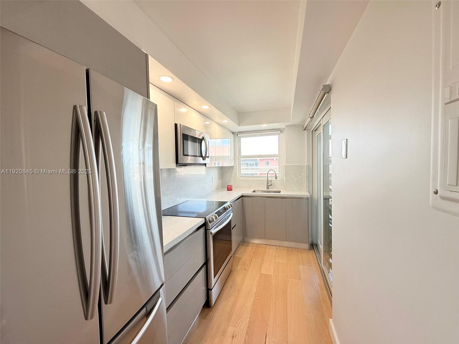 A modern galley kitchen features stainless steel appliances, light gray cabinets, and light wood flooring — 180 NE 12th Ave # 12E, Hallandale Beach FL 33009, HALLANDALE BEACH, FL