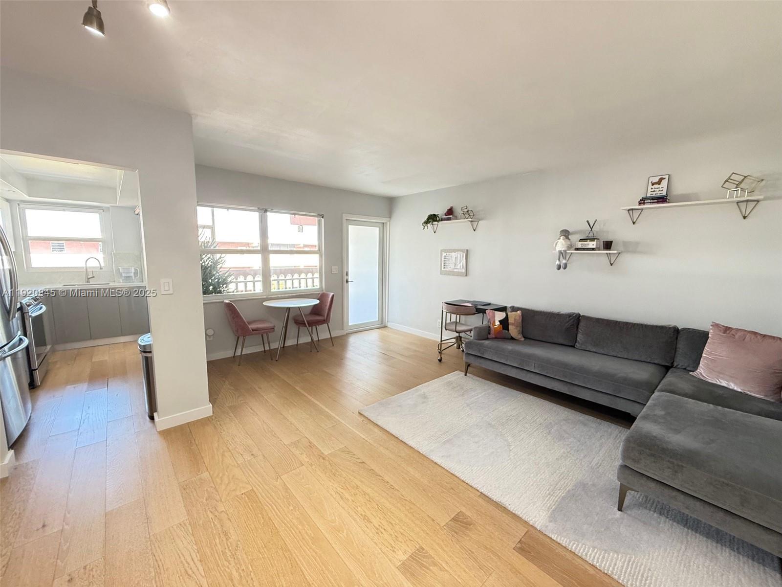 A living room with light wood floors, a gray sectional sofa, and an adjacent kitchen — 180 NE 12th Ave # 12E, Hallandale Beach FL 33009, HALLANDALE BEACH, FL