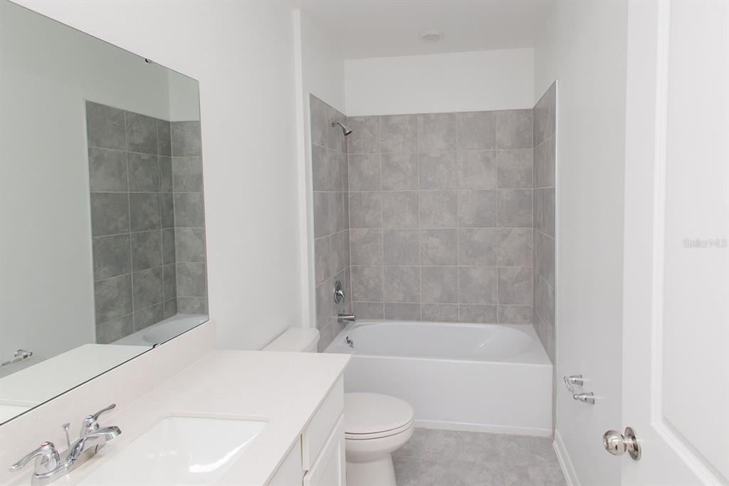 A bathroom features a white vanity, a toilet, and a tub-shower combo with gray tiles — 1482 AUSTIN STREET, WINTER HAVEN, FL