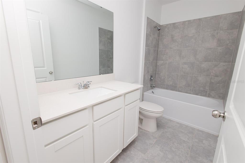 A bathroom features a white vanity, a mirror, a toilet, and a tiled shower-tub combination — 1482 AUSTIN STREET, WINTER HAVEN, FL