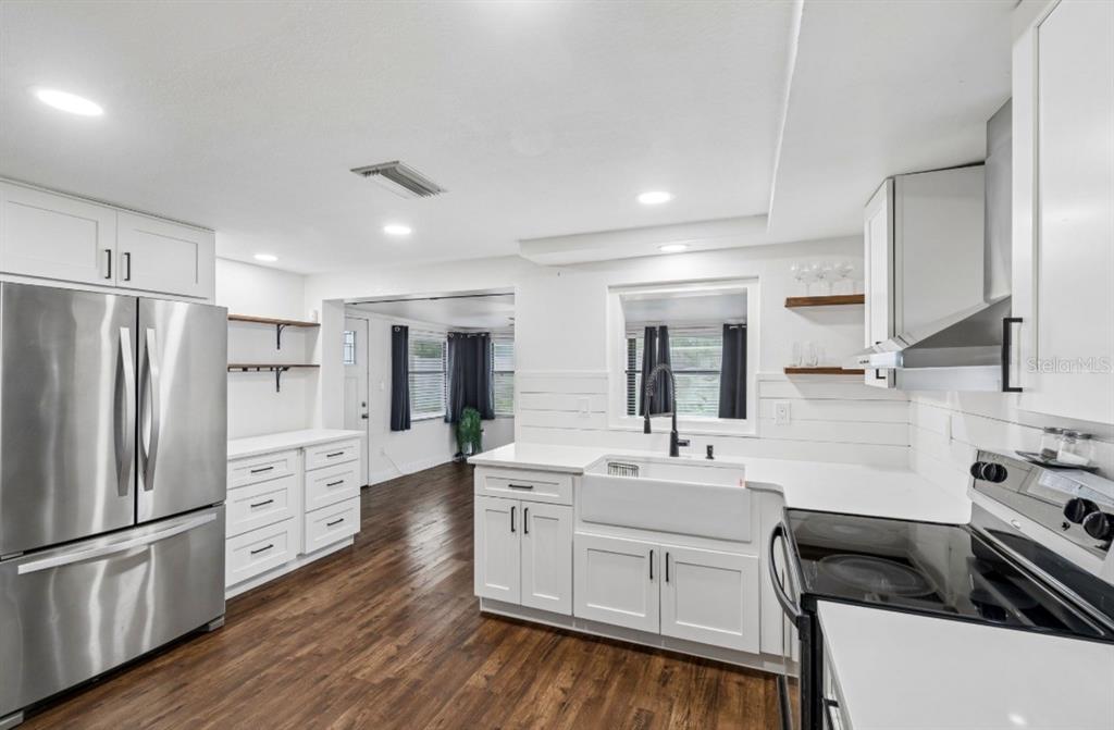 A modern kitchen features white cabinets, stainless steel appliances, a farmhouse sink, and wood flooring — 4531 KENNEDY DRIVE, NEW PORT RICHEY, FL